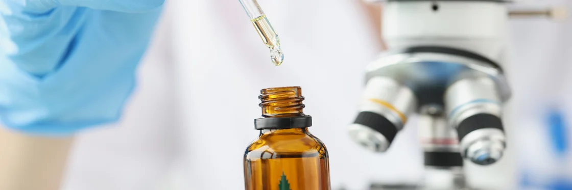 A gloved hand using a pipette above a medicine bottle beside a microscope A gloved hand using a pipette above a medicine bottle beside a microscope